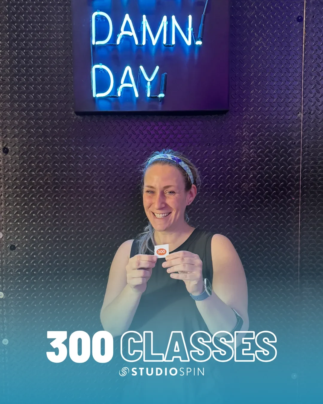 A Studio Spin member celebrating 300 classes under the Every Damn Day neon sign.