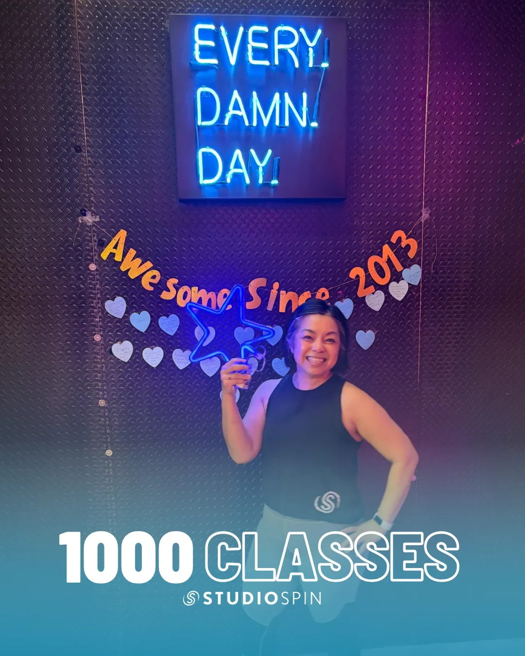 A Studio Spin member celebrating 1,000 classes under the Every Damn Day neon sign.