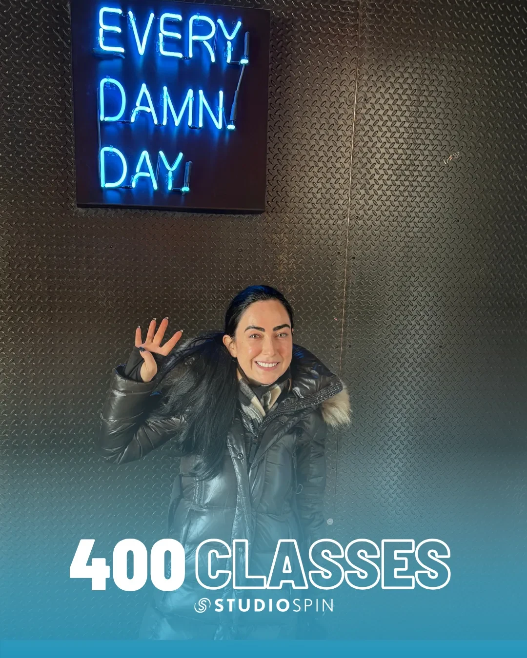 A Studio Spin member celebrating 400 classes under the Every Damn Day neon sign.