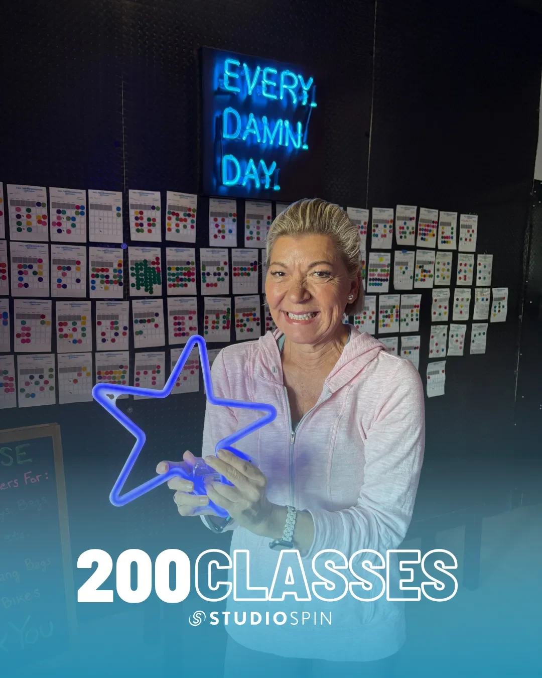 A Studio Spin member celebrating 200 classes under the Every Damn Day neon sign.