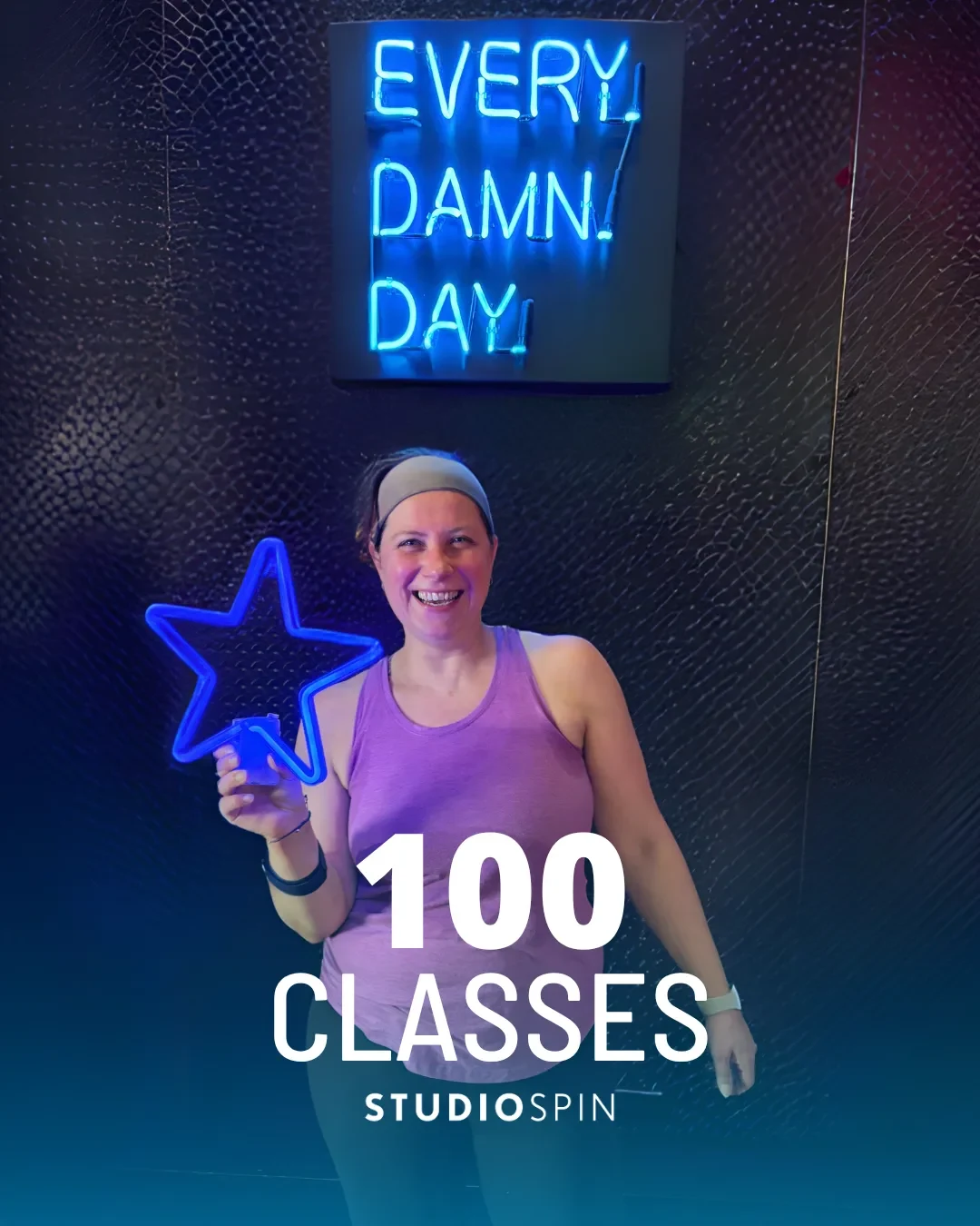 A Studio Spin member celebrating 100 classes under the Every Damn Day neon sign.