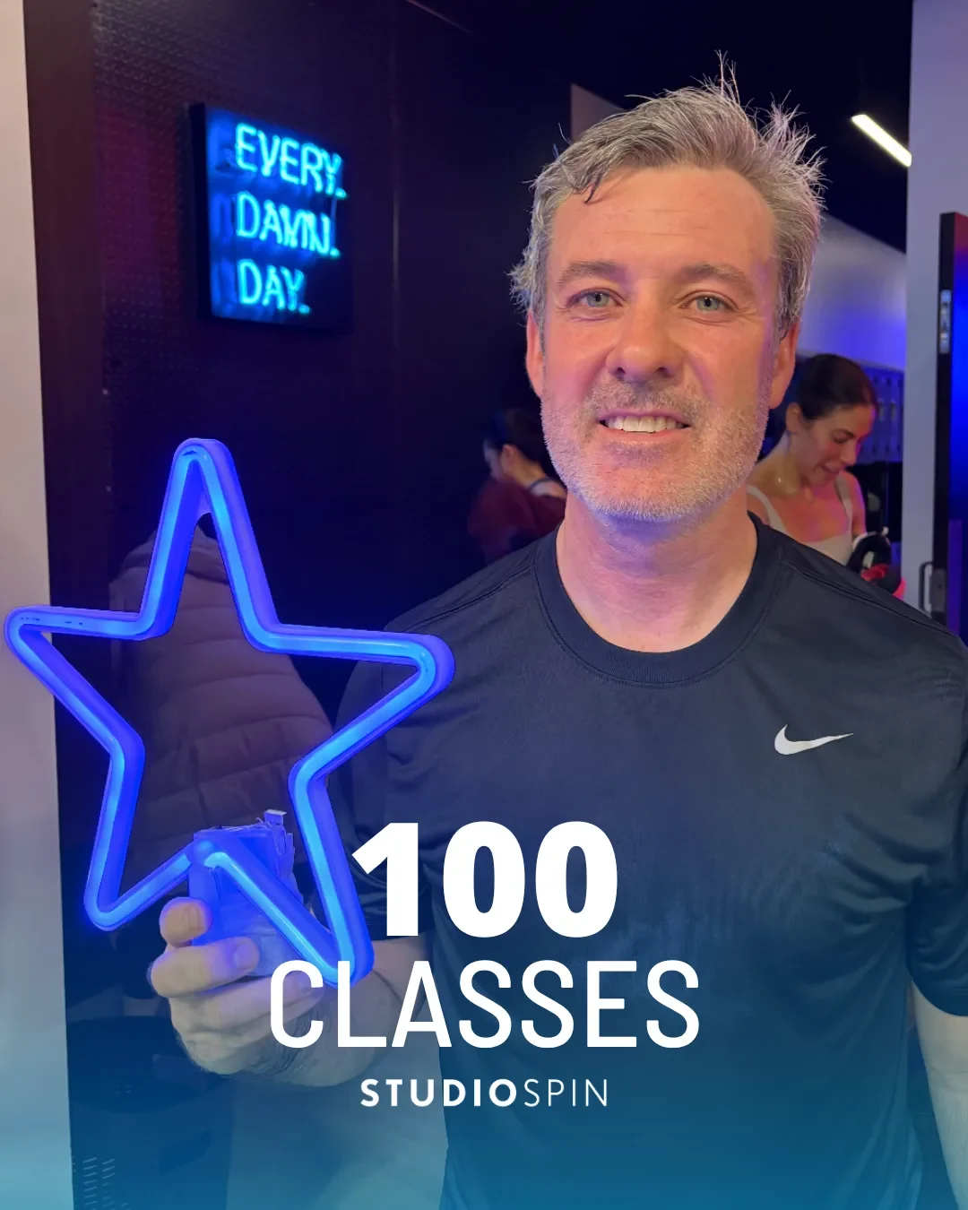 A Studio Spin member celebrating 100 classes under the Every Damn Day neon sign.