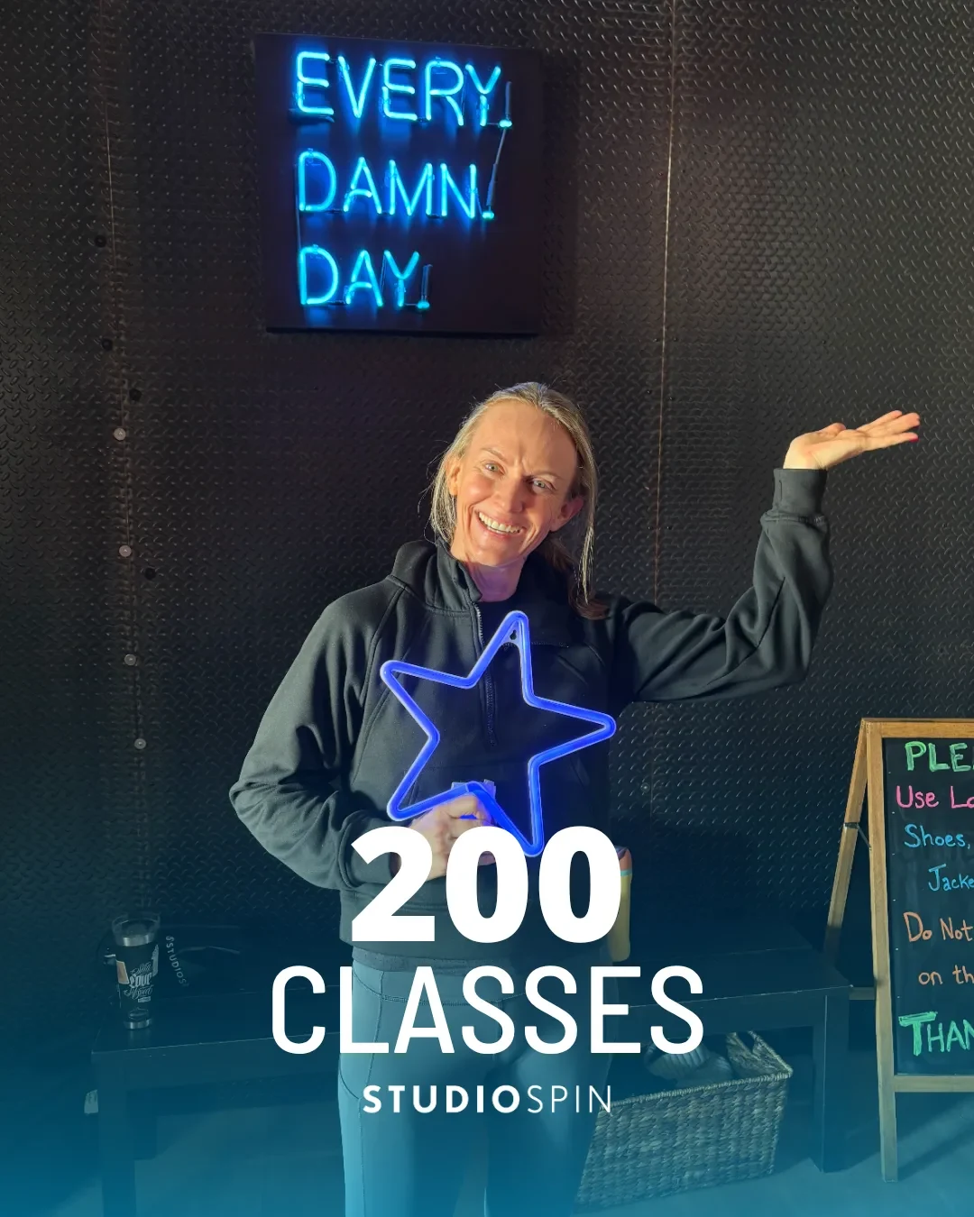 A Studio Spin member celebrating 200 classes under the Every Damn Day neon sign.