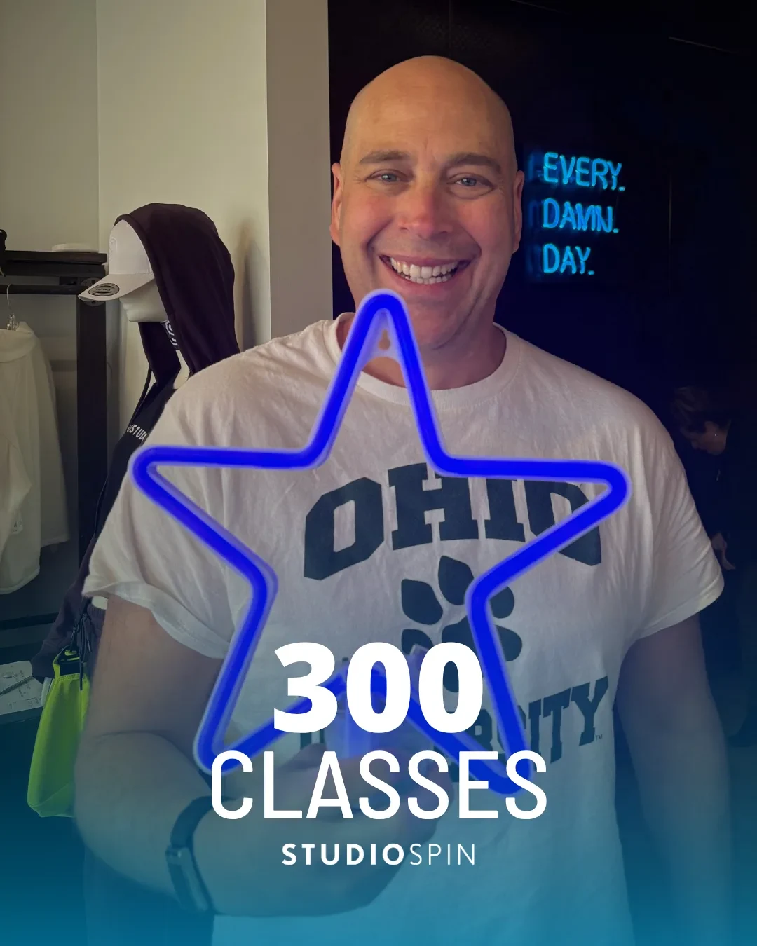 A Studio Spin member celebrating 300 classes under the Every Damn Day neon sign.
