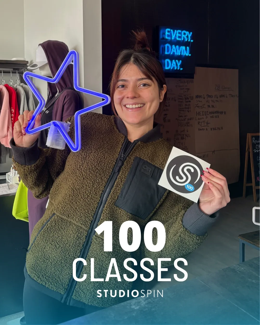 A Studio Spin member celebrating 100 classes under the Every Damn Day neon sign.