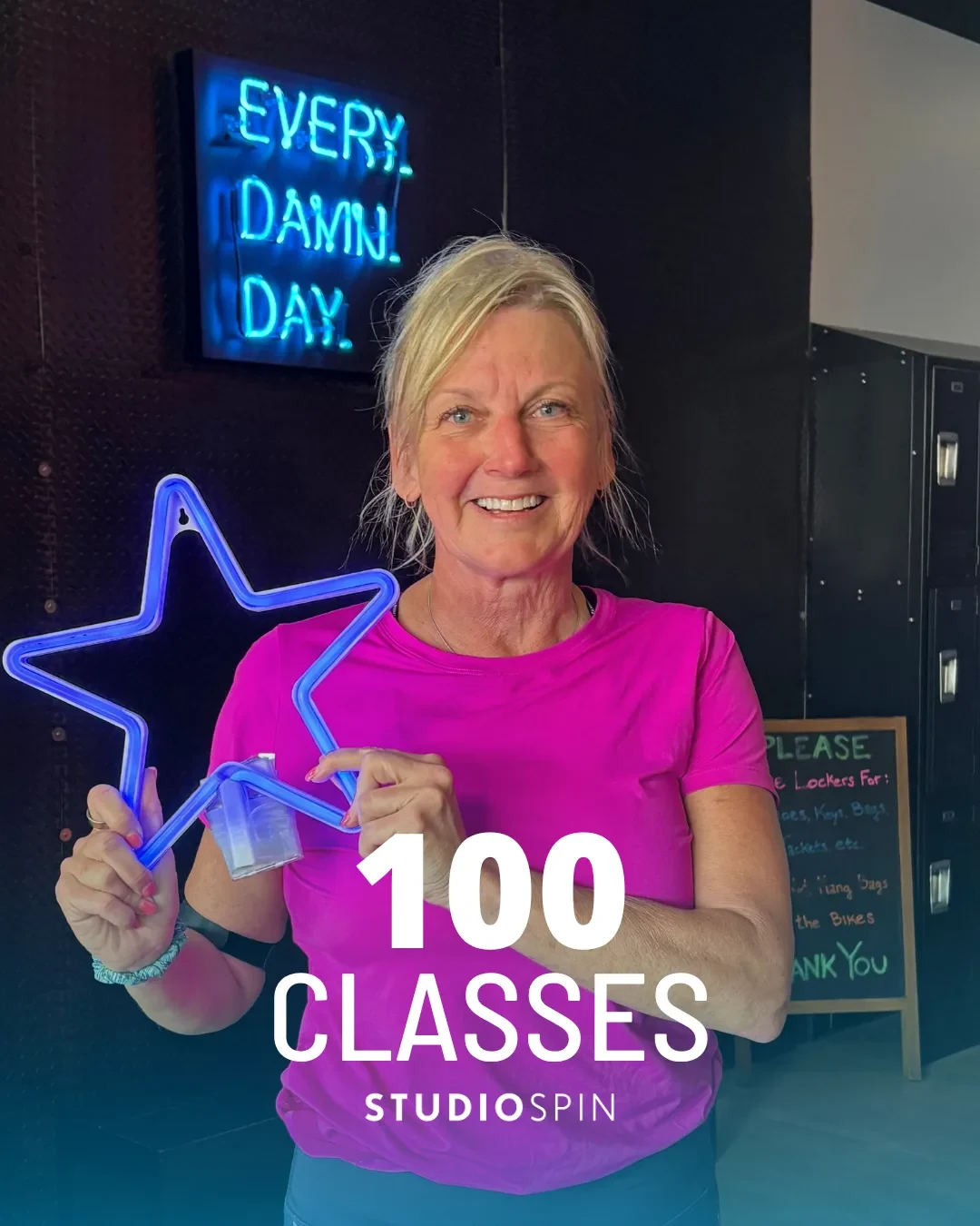 A Studio Spin member celebrating 100 classes under the Every Damn Day neon sign.
