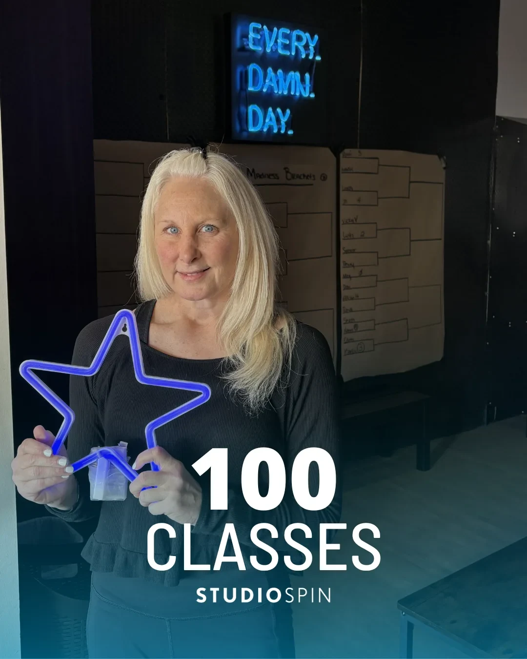 A Studio Spin member celebrating 100 classes under the Every Damn Day neon sign.