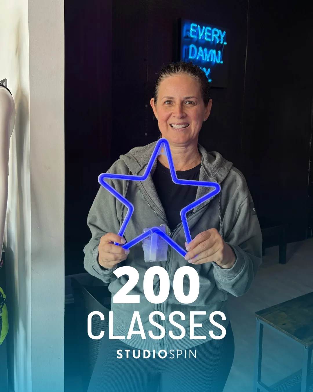A Studio Spin member celebrating 200 classes under the Every Damn Day neon sign.