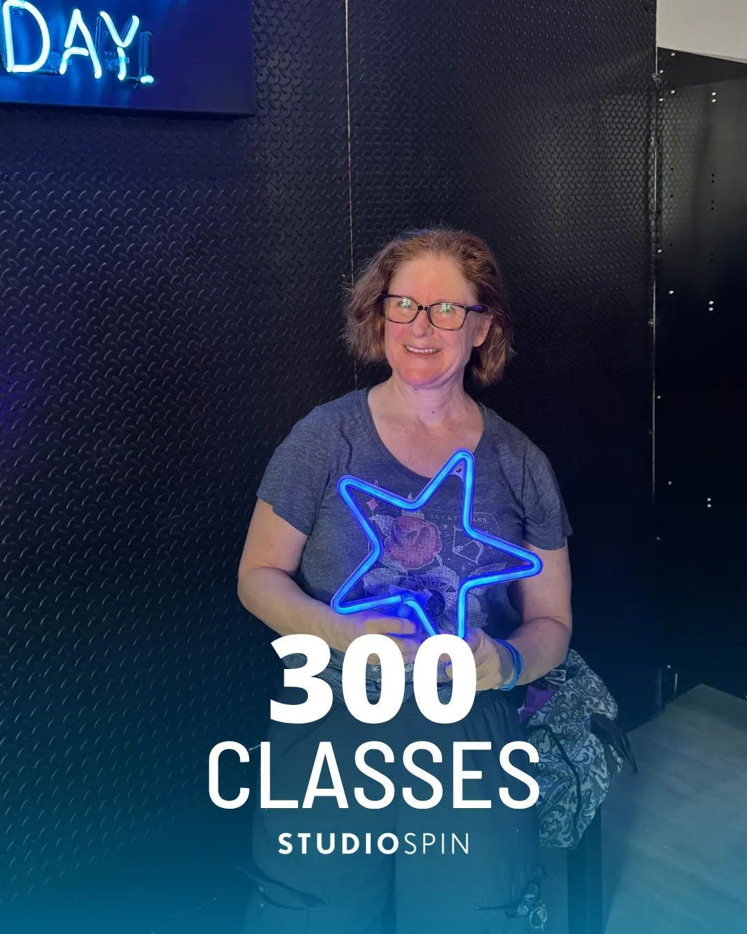 A Studio Spin member celebrating 300 classes under the Every Damn Day neon sign.