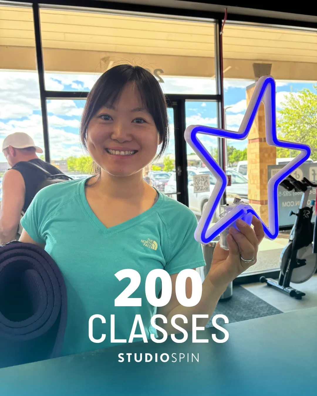 A Studio Spin member celebrating 200 classes under the Every Damn Day neon sign.