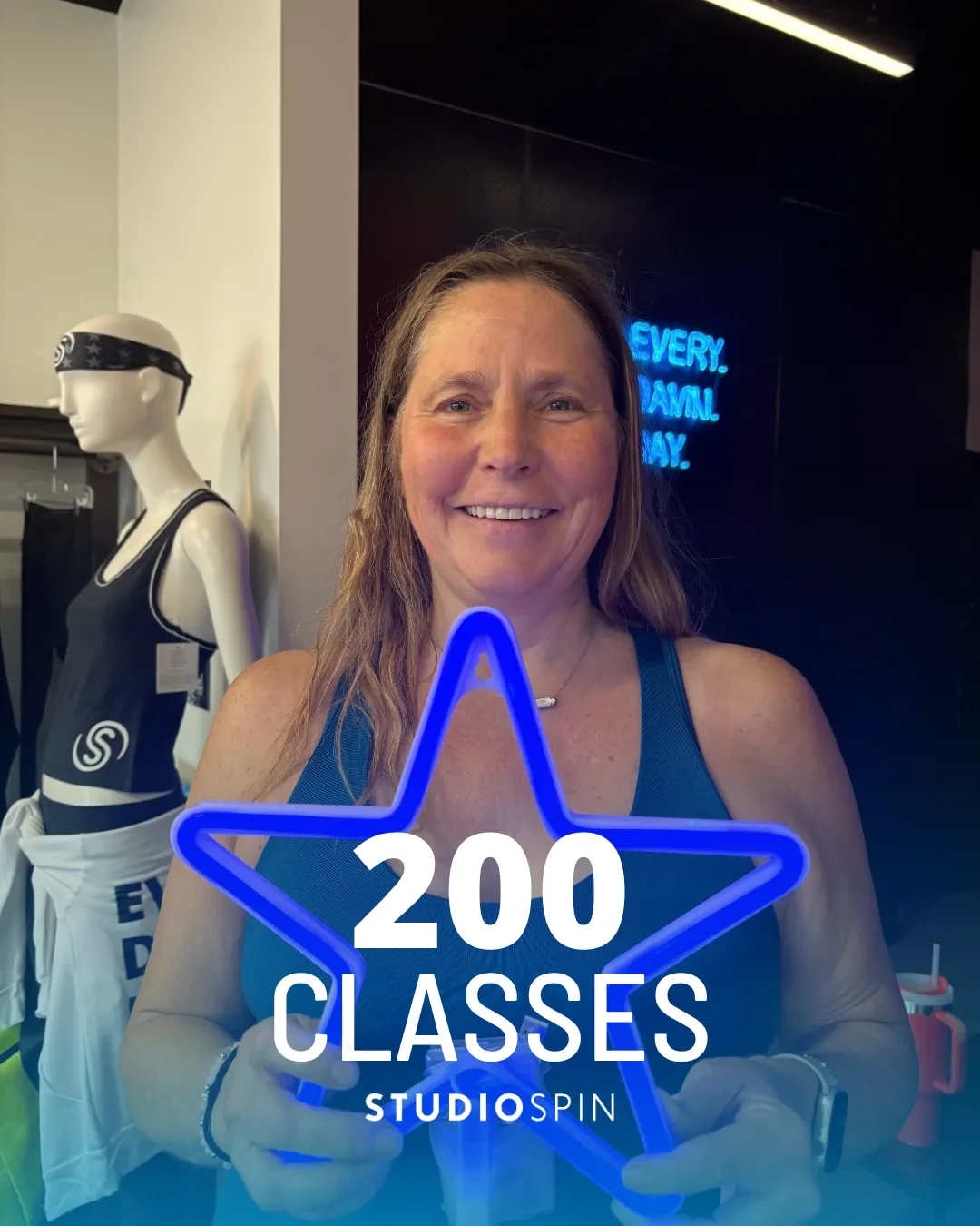A Studio Spin member celebrating 200 classes under the Every Damn Day neon sign.
