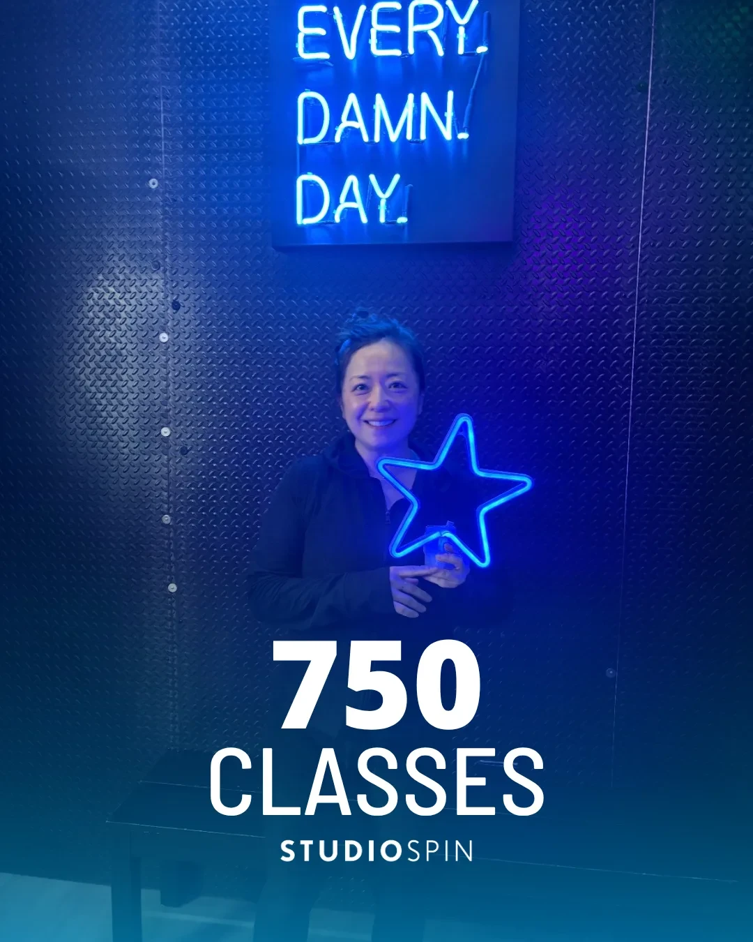 A Studio Spin member celebrating 750 classes under the Every Damn Day neon sign.