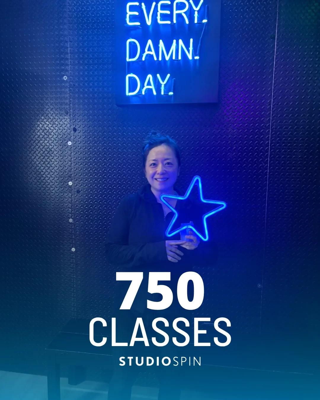 A Studio Spin member celebrating 750 classes under the Every Damn Day neon sign.