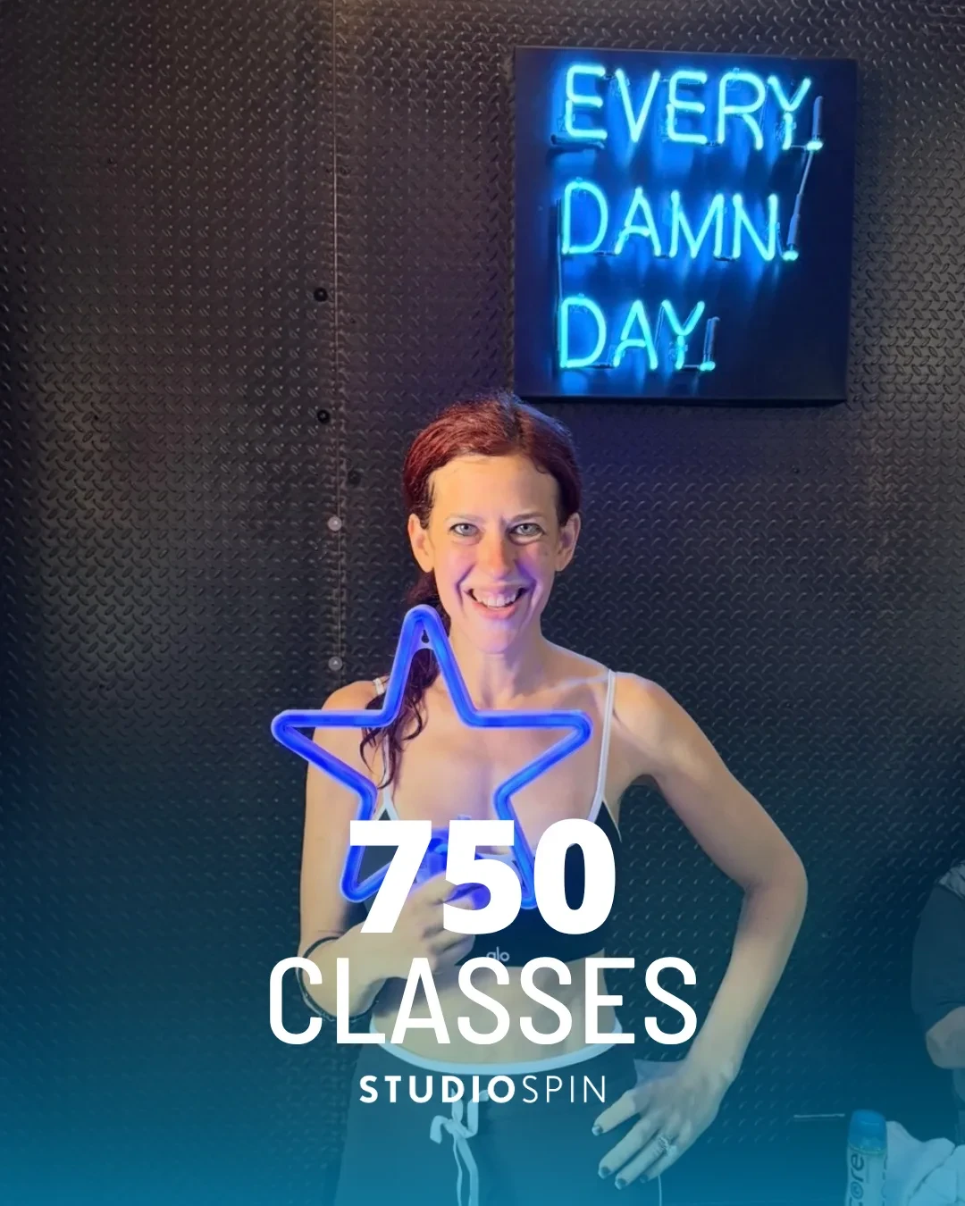 A Studio Spin member celebrating 750 classes under the Every Damn Day neon sign.