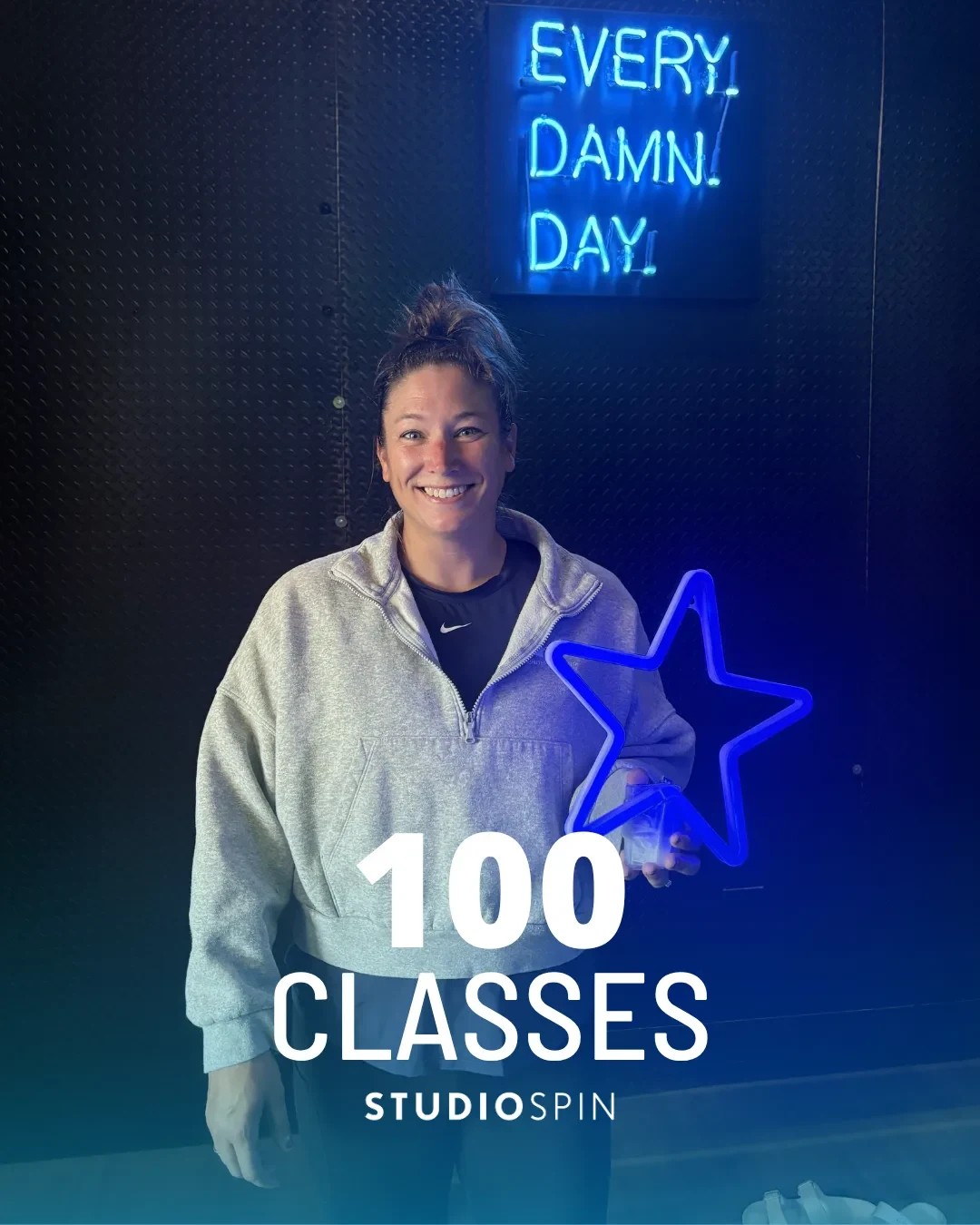 A Studio Spin member celebrating 100 classes under the Every Damn Day neon sign.