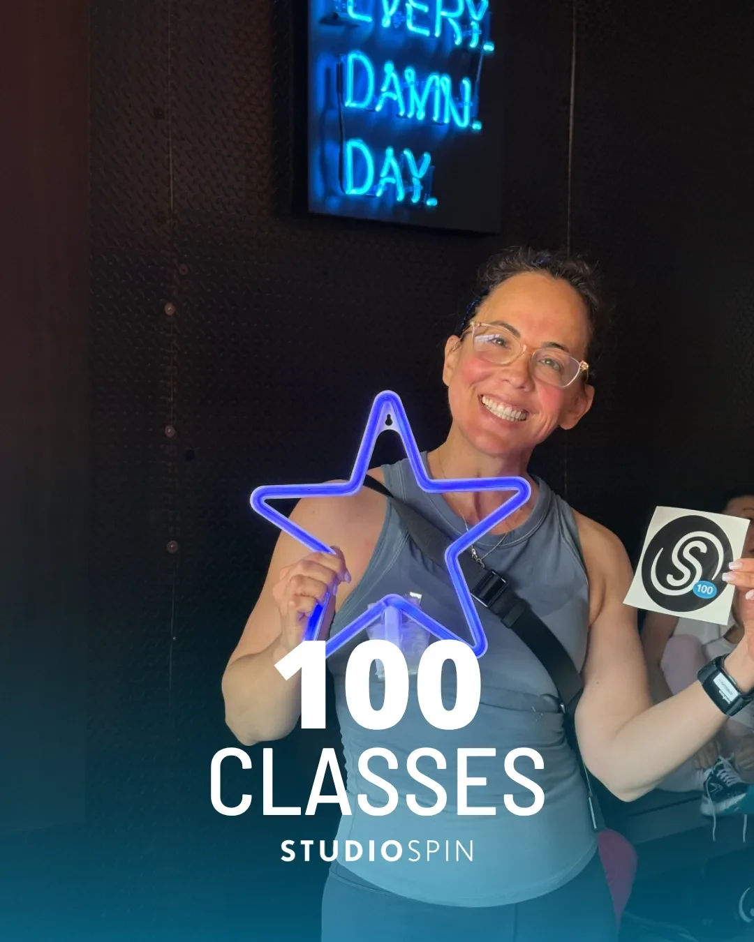 A Studio Spin member celebrating 100 classes under the Every Damn Day neon sign.