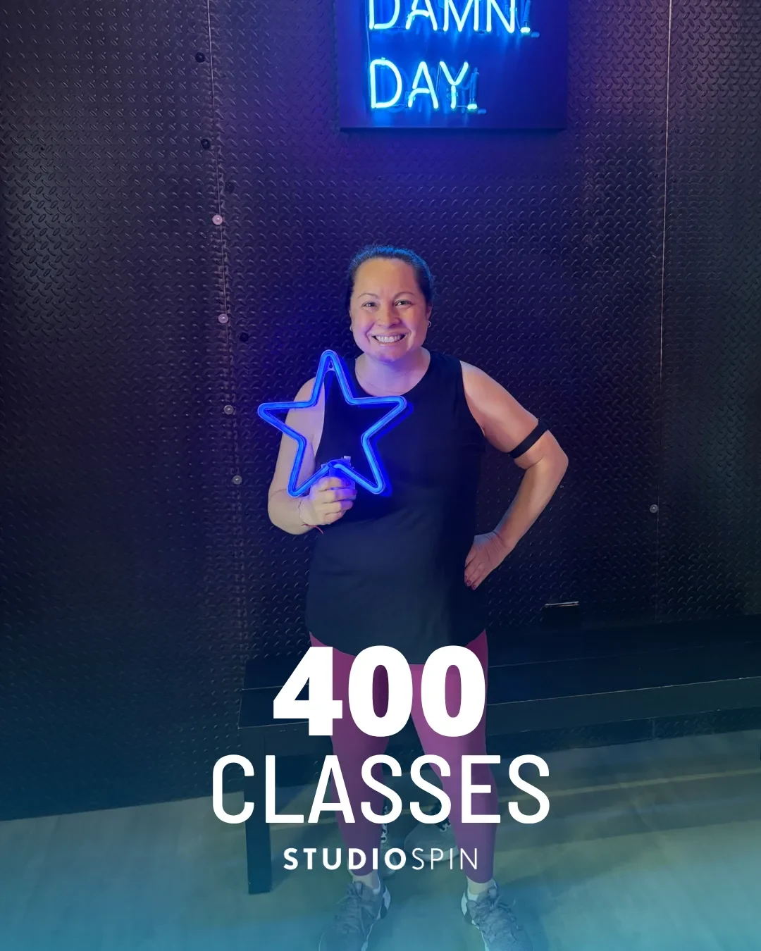 A Studio Spin member celebrating 400 classes under the Every Damn Day neon sign.