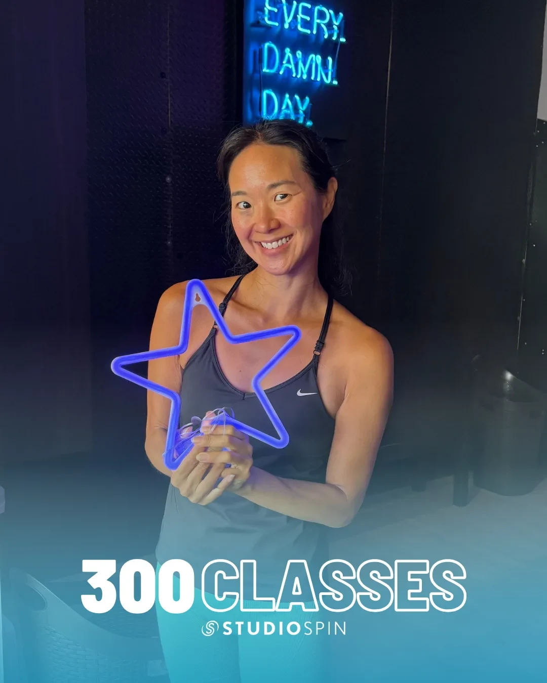 A Studio Spin member celebrating 300 classes under the Every Damn Day neon sign.