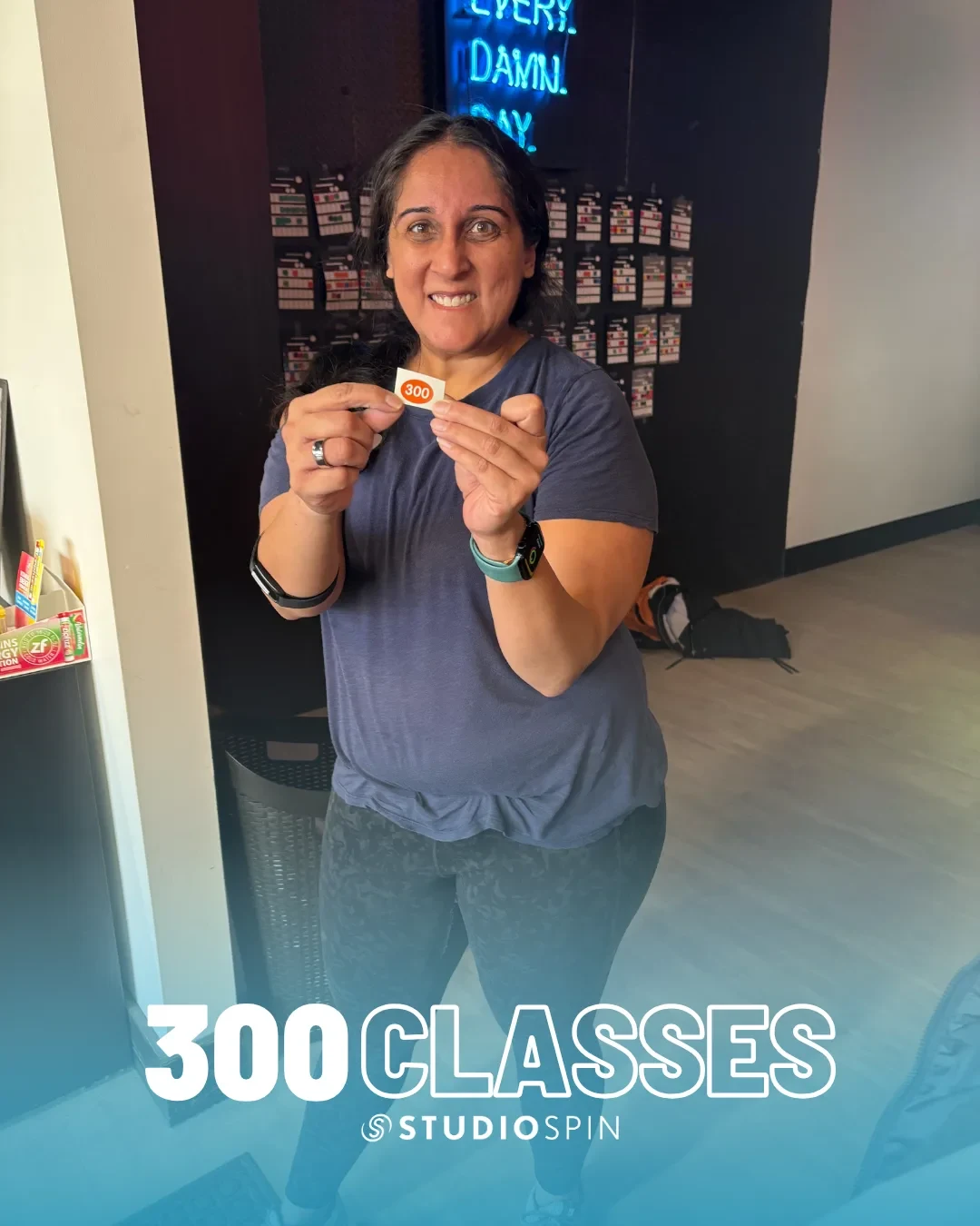 A Studio Spin member celebrating 300 classes under the Every Damn Day neon sign.