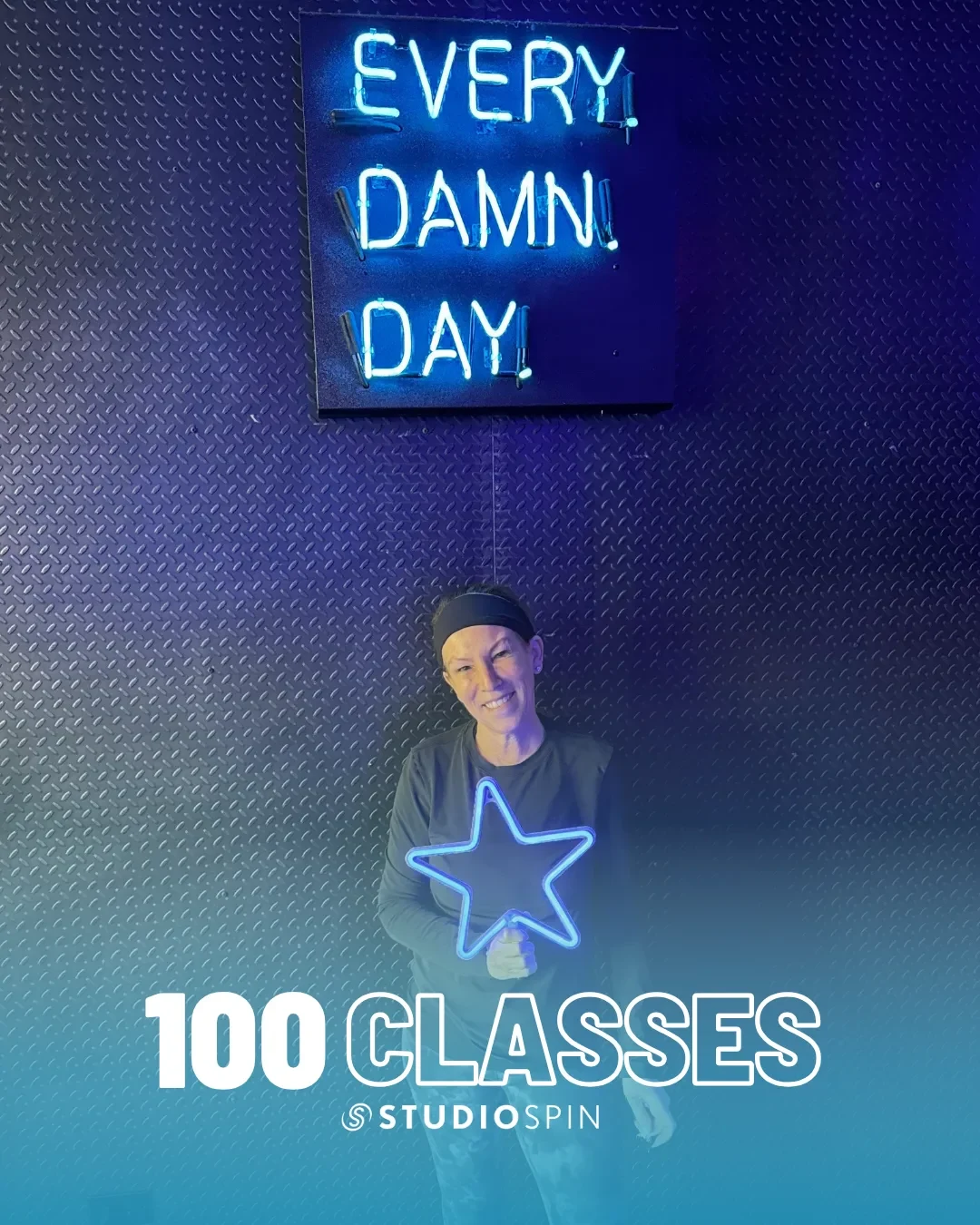 A Studio Spin member celebrating 100 classes under the Every Damn Day neon sign.
