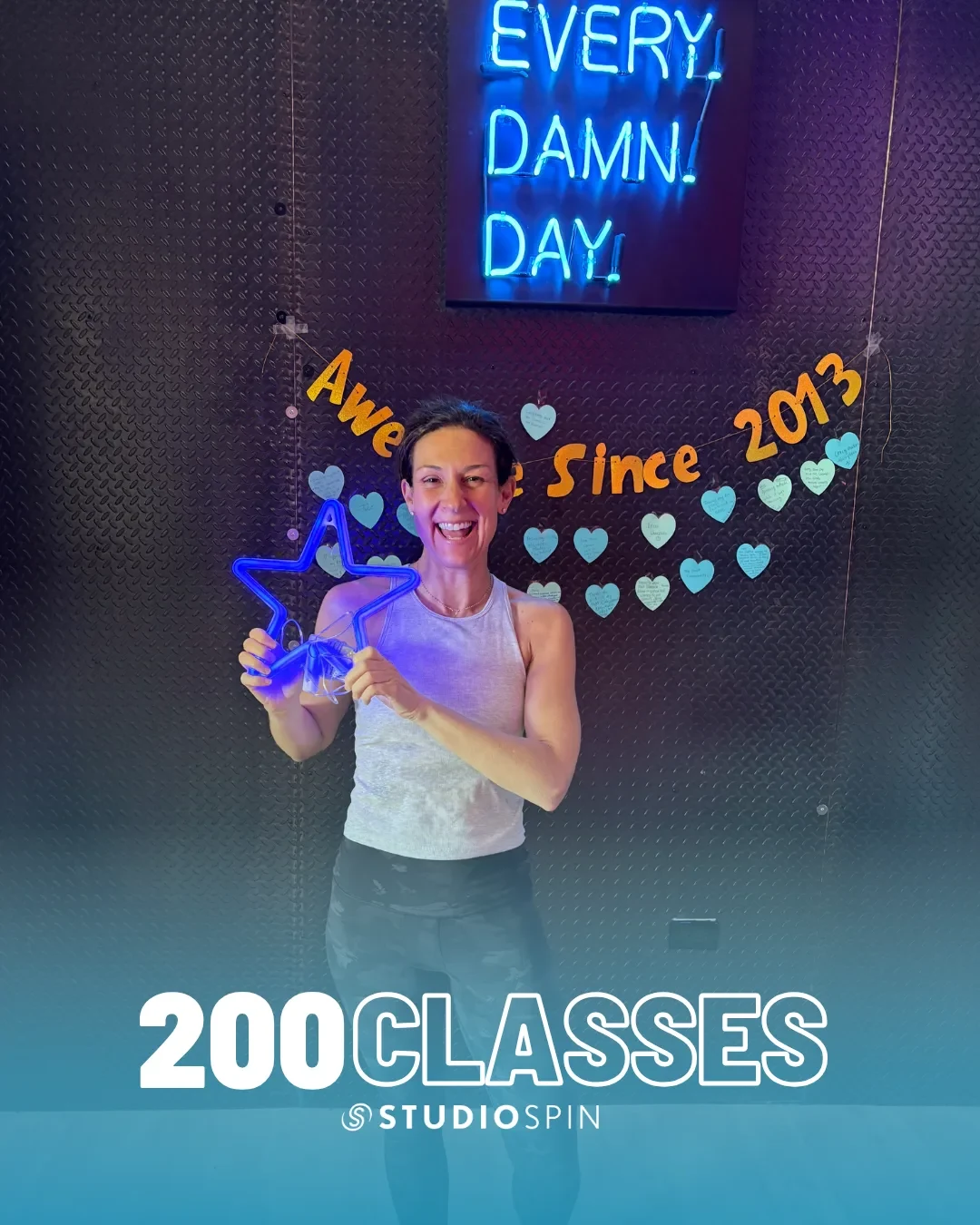 A Studio Spin member celebrating 200 classes under the Every Damn Day neon sign.