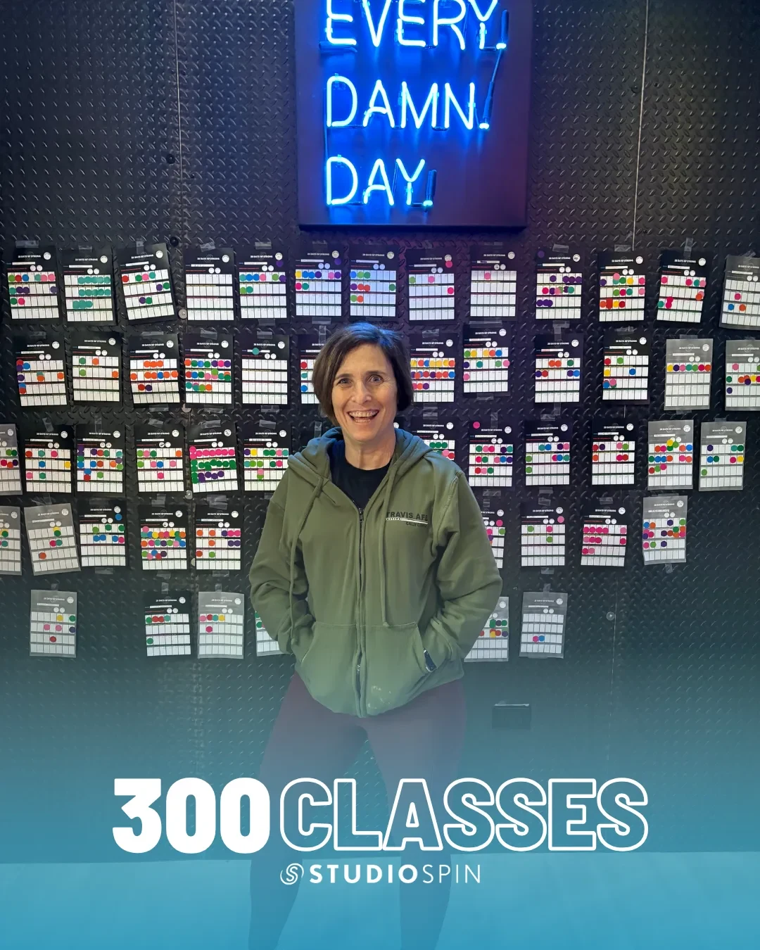 A Studio Spin member celebrating 300 classes under the Every Damn Day neon sign.