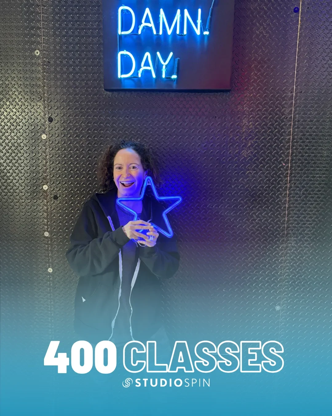 A Studio Spin member celebrating 400 classes under the Every Damn Day neon sign.