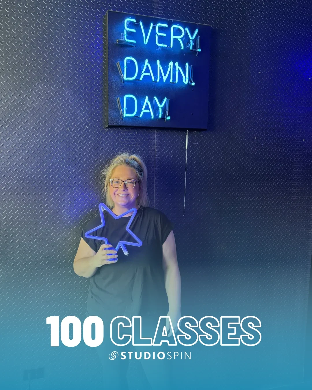 A Studio Spin member celebrating 100 classes under the Every Damn Day neon sign.