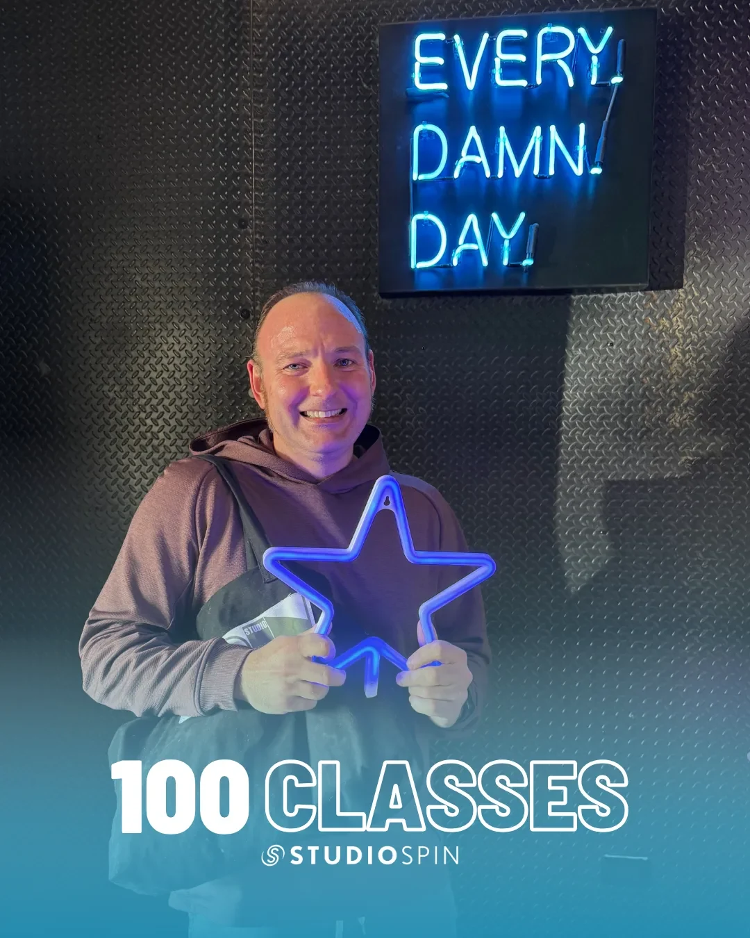 A Studio Spin member celebrating 100 classes under the Every Damn Day neon sign.