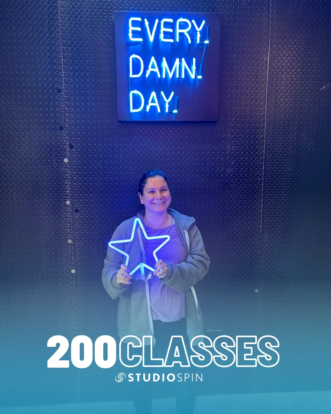 A Studio Spin member celebrating 200 classes under the Every Damn Day neon sign.