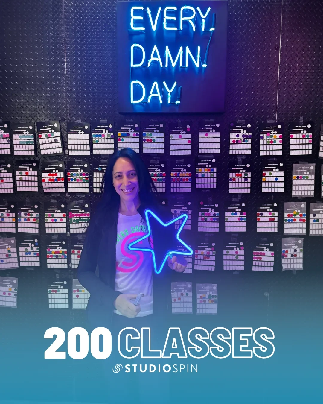 A Studio Spin member celebrating 200 classes under the Every Damn Day neon sign.