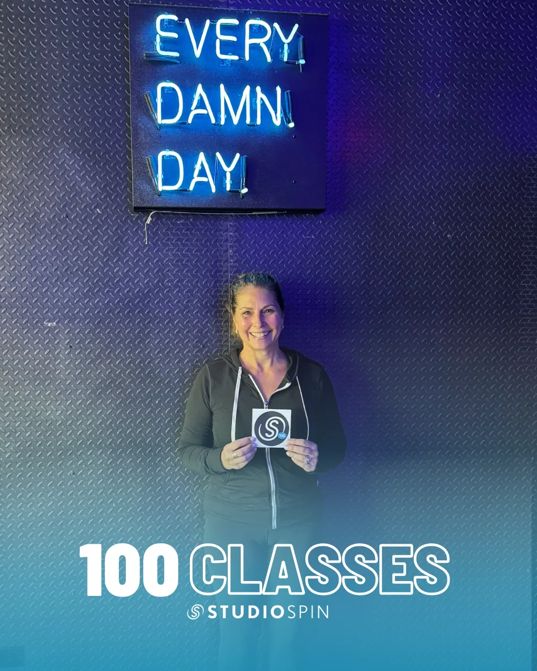 A Studio Spin member celebrating 100 classes under the Every Damn Day neon sign.