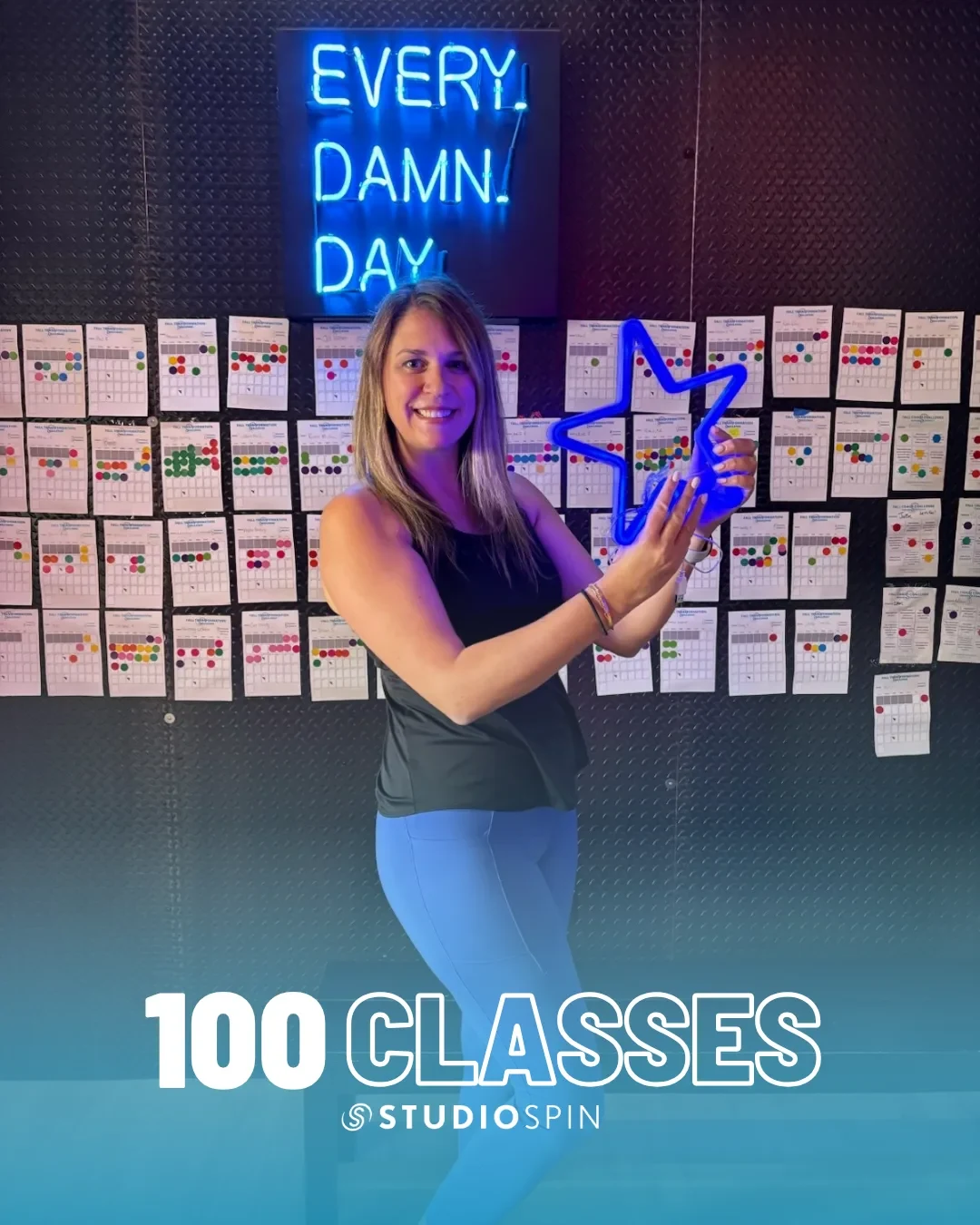 A Studio Spin member celebrating 100 classes under the Every Damn Day neon sign.