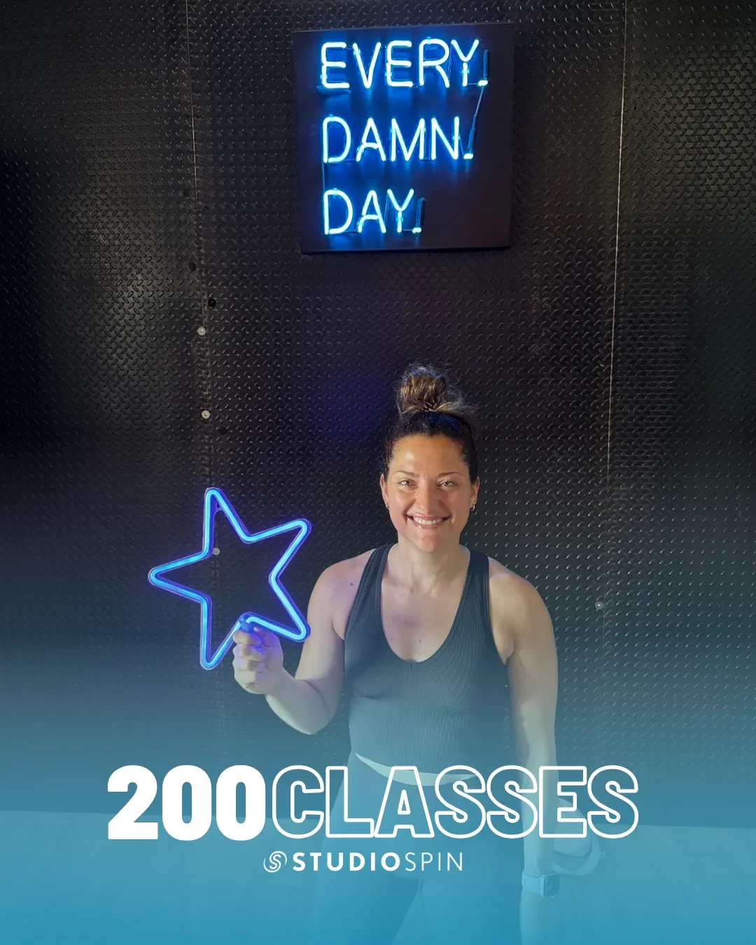A Studio Spin member celebrating 200 classes under the Every Damn Day neon sign.