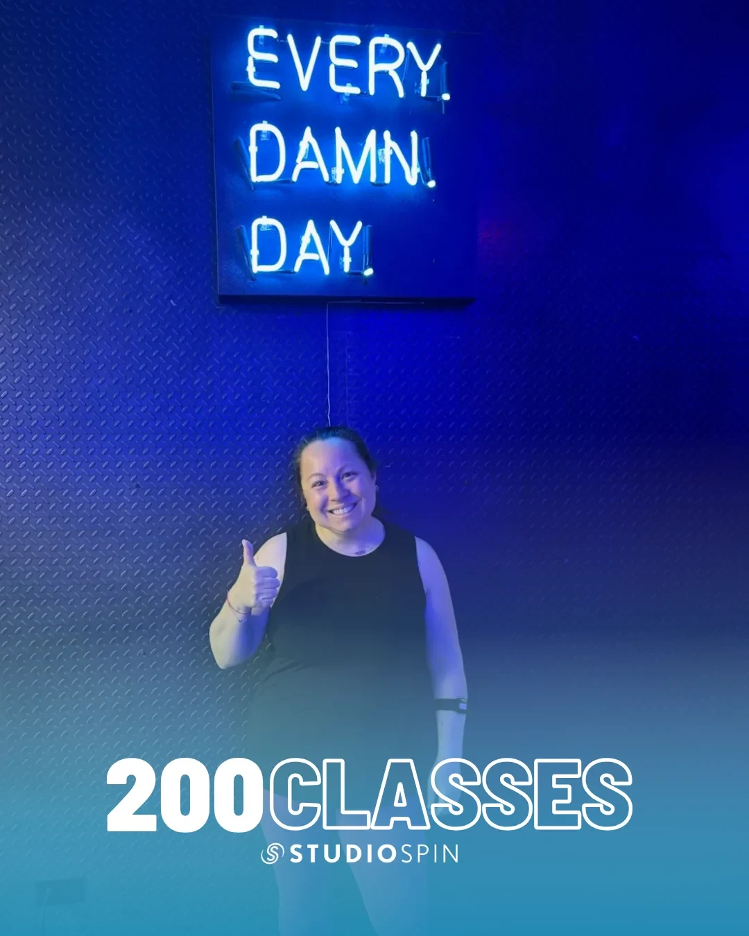 A Studio Spin member celebrating 200 classes under the Every Damn Day neon sign.