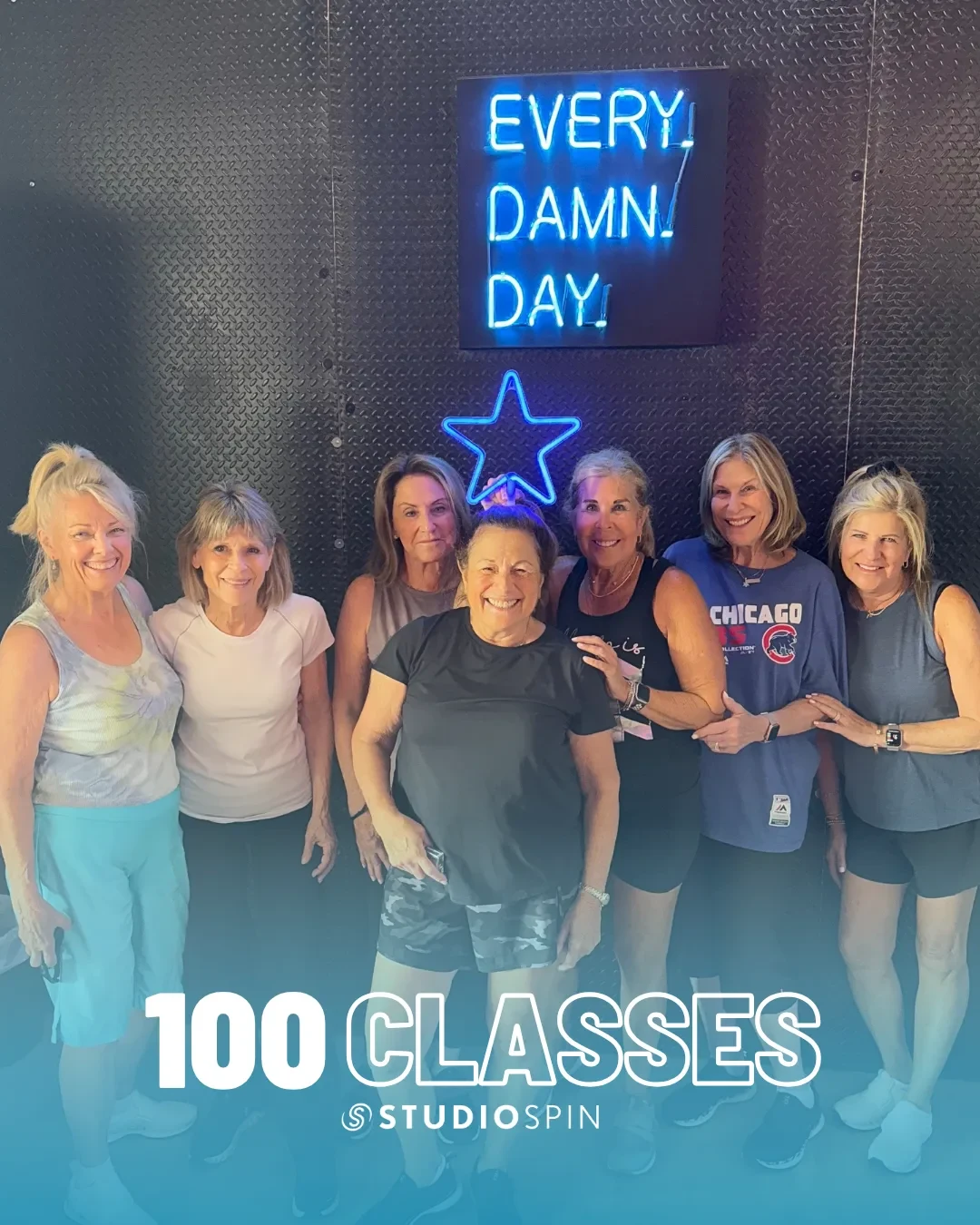 A Studio Spin member celebrating 100 classes under the Every Damn Day neon sign.