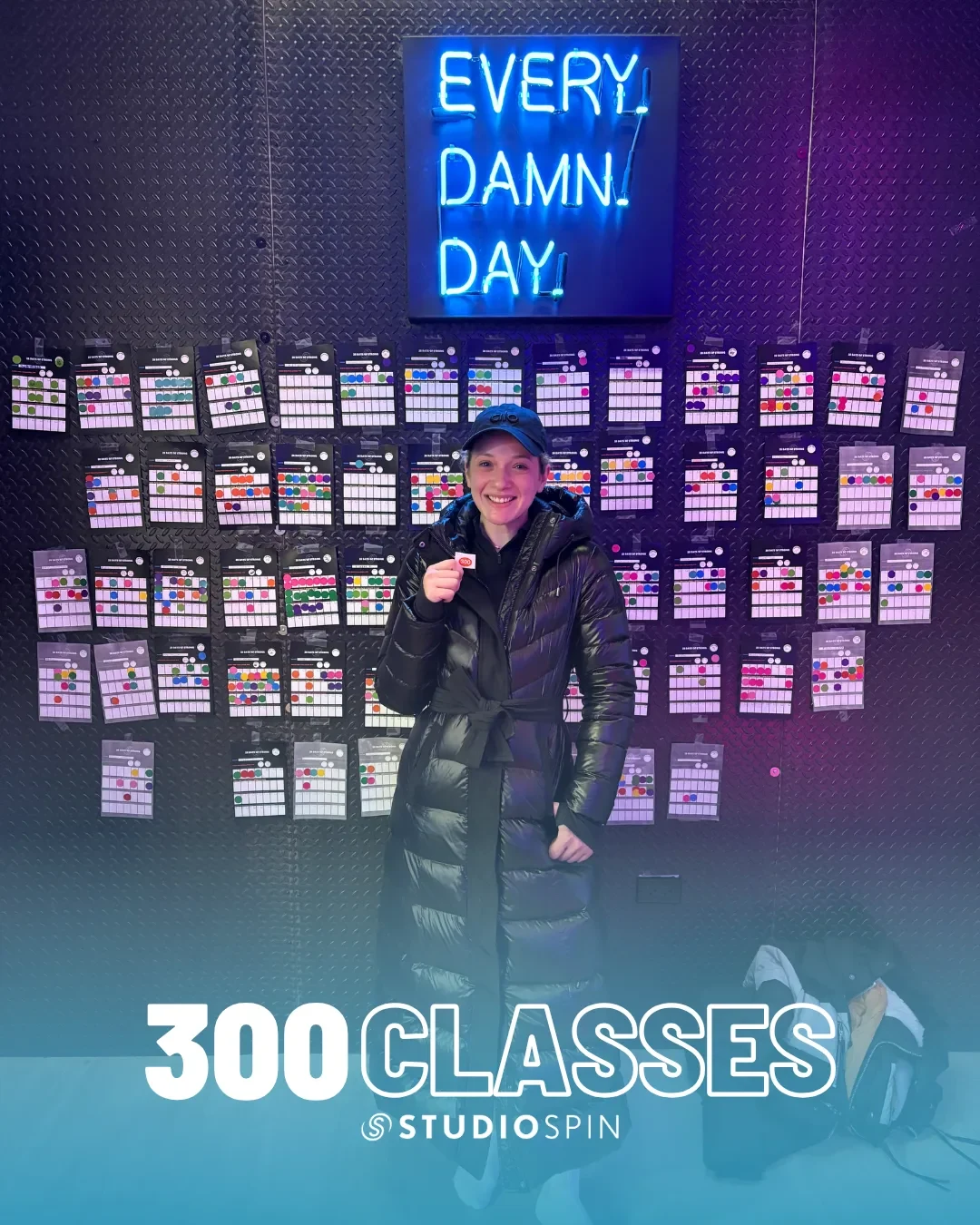 A Studio Spin member celebrating 300 classes under the Every Damn Day neon sign.