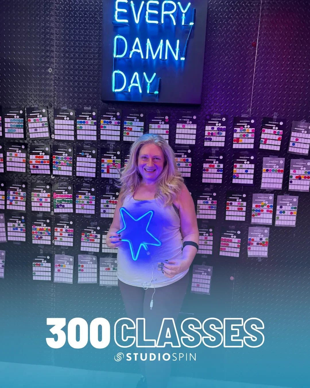 A Studio Spin member celebrating 300 classes under the Every Damn Day neon sign.