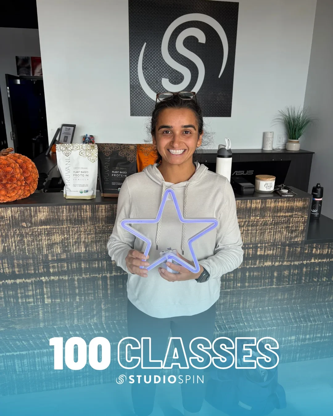 A Studio Spin member celebrating 100 classes under the Every Damn Day neon sign.