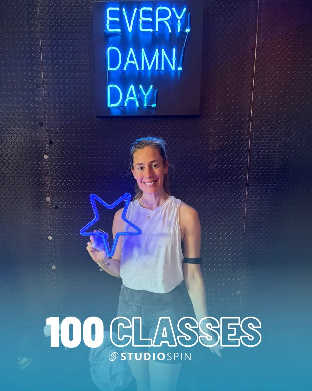 A Studio Spin member celebrating 100 classes under the Every Damn Day neon sign.