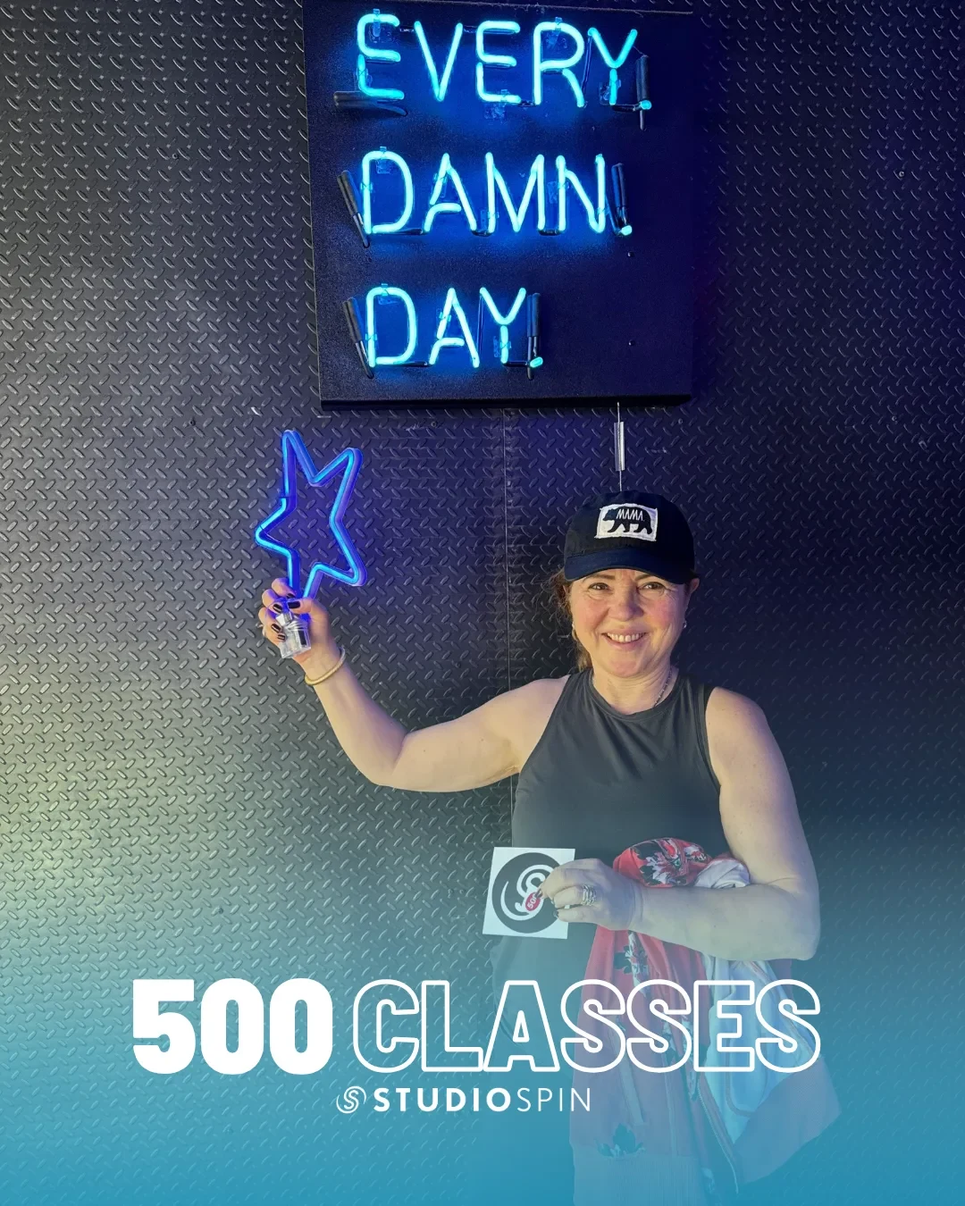 A Studio Spin member celebrating 500 classes under the Every Damn Day neon sign.