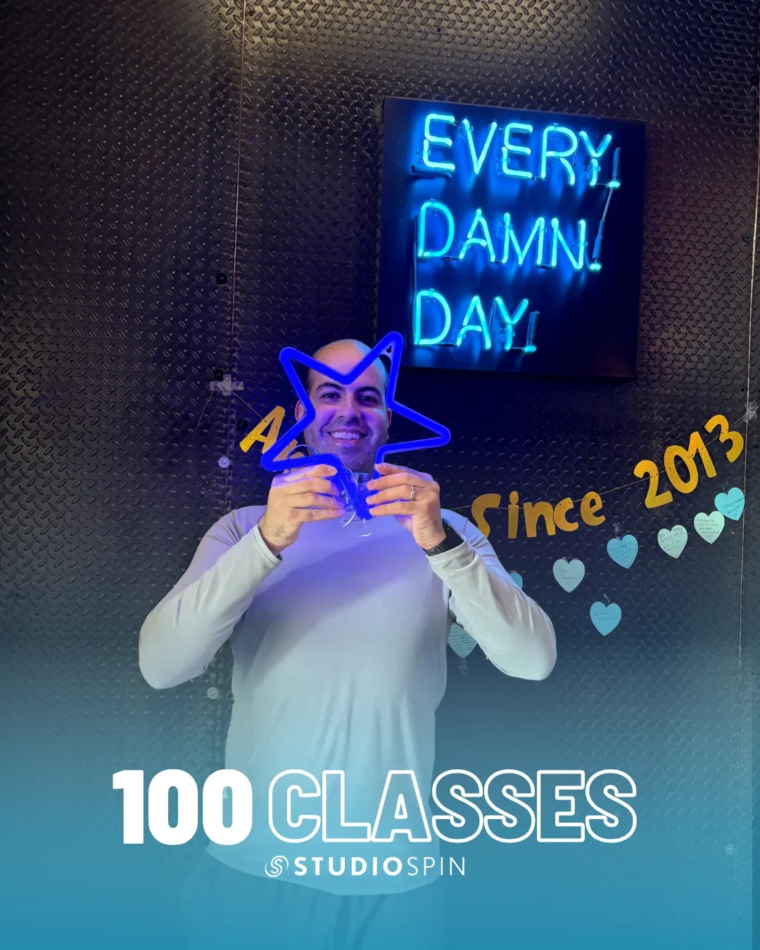 A Studio Spin member celebrating 100 classes under the Every Damn Day neon sign.