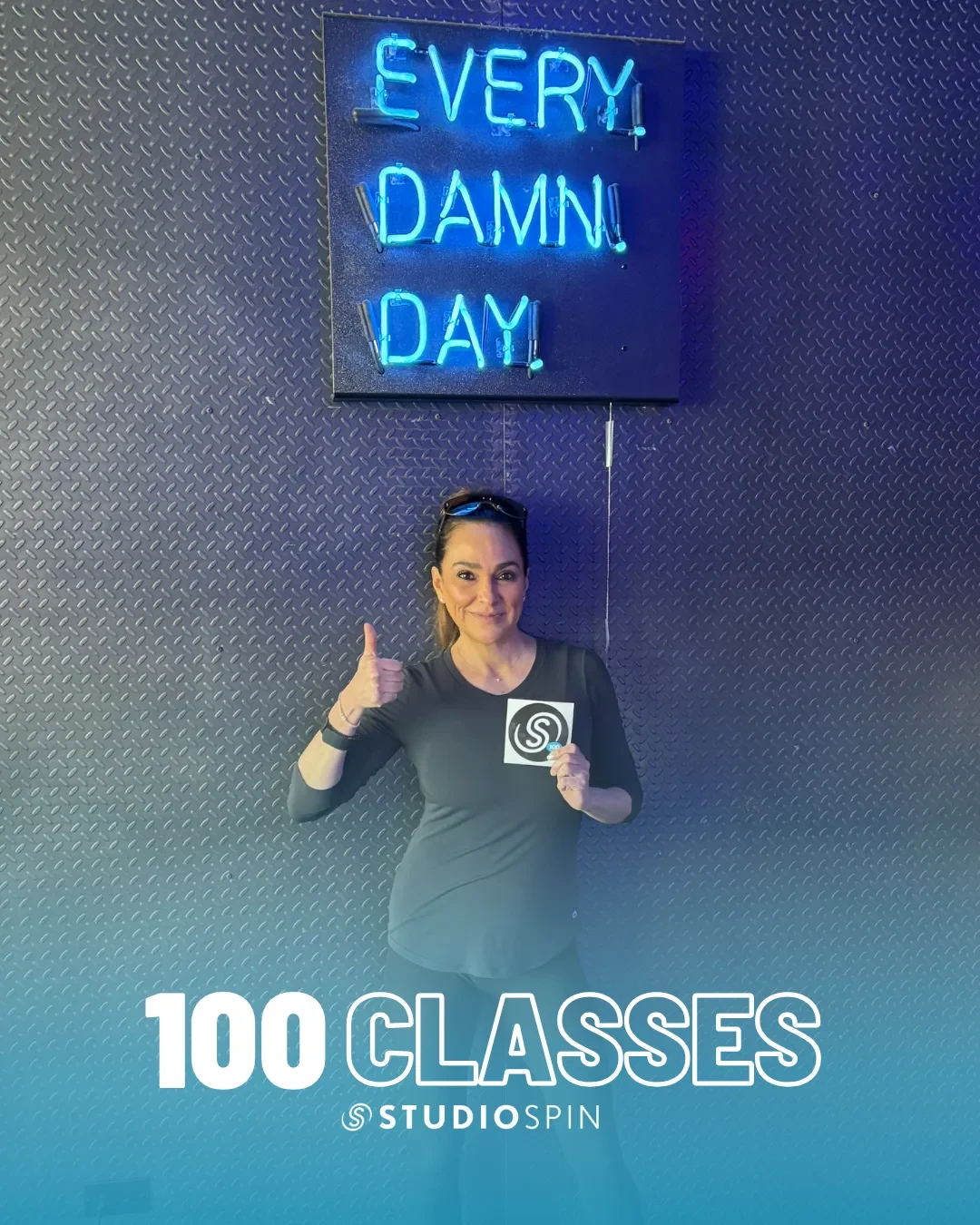 A Studio Spin member celebrating 100 classes under the Every Damn Day neon sign.