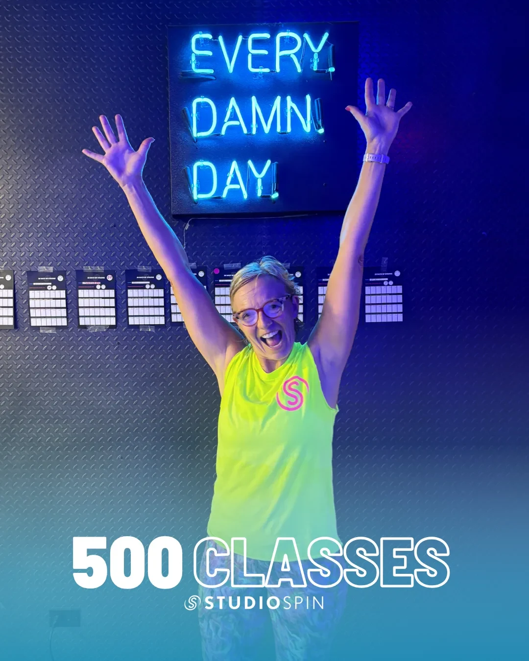 A Studio Spin member celebrating 500 classes under the Every Damn Day neon sign.