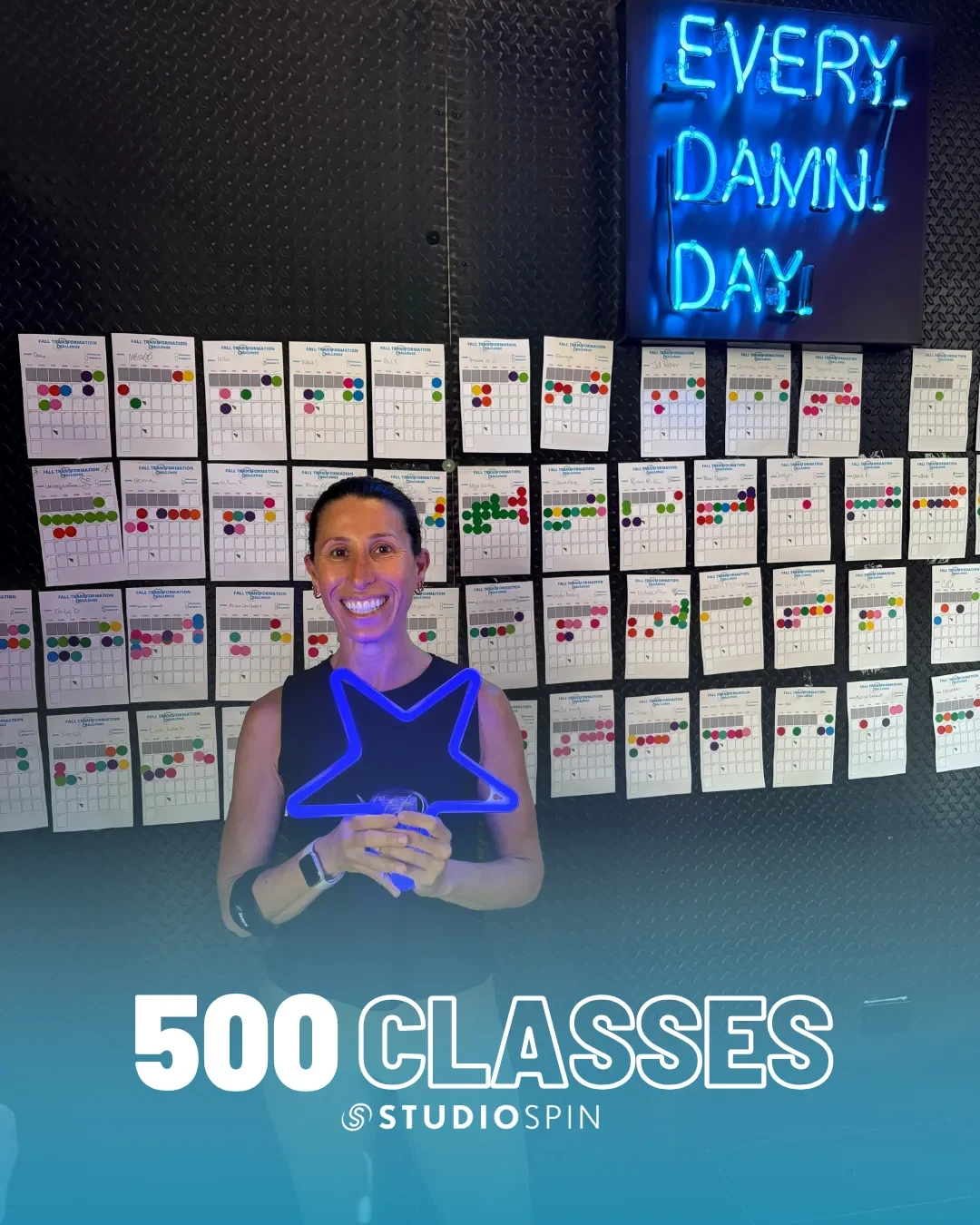 A Studio Spin member celebrating 500 classes under the Every Damn Day neon sign.