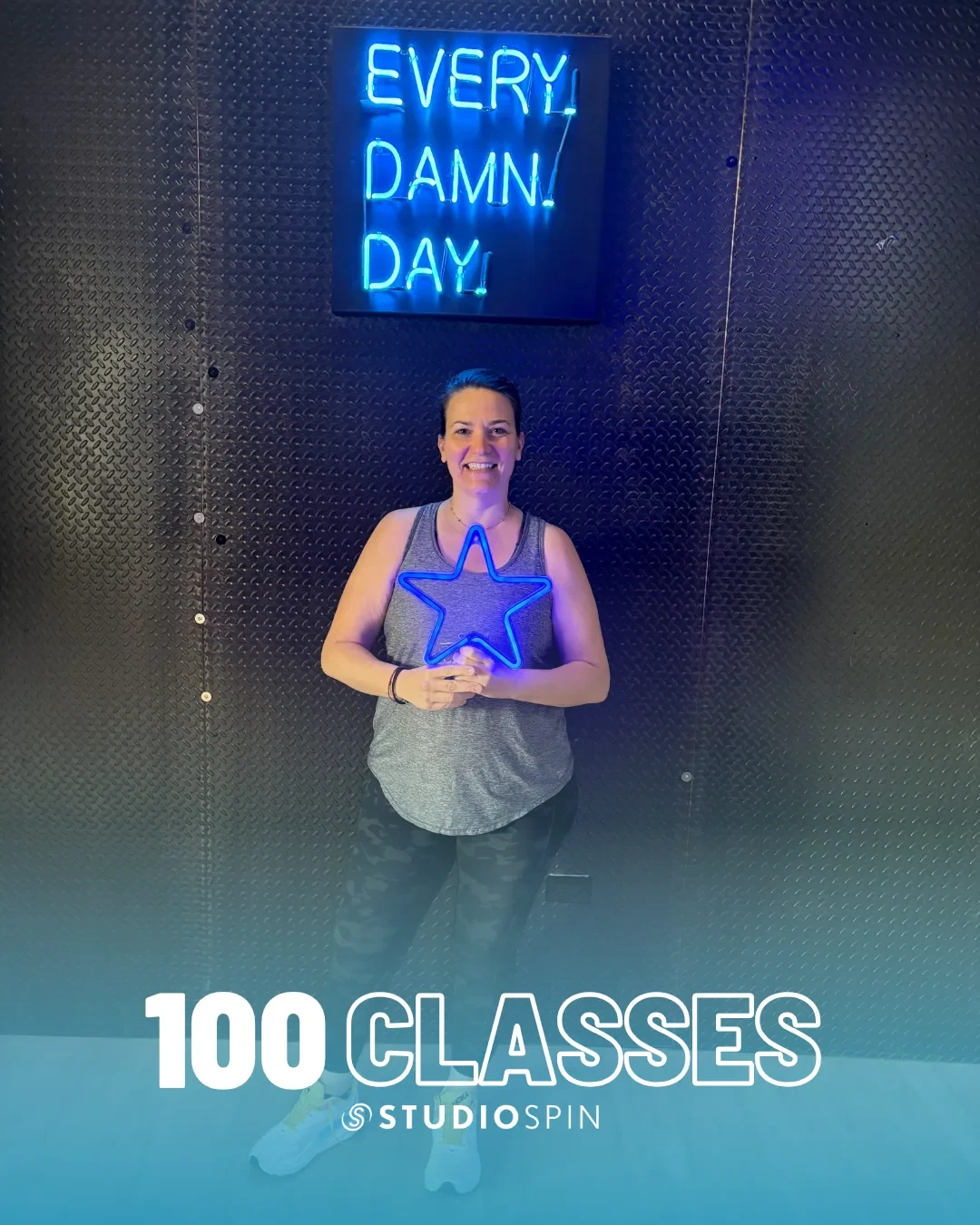A Studio Spin member celebrating 100 classes under the Every Damn Day neon sign.