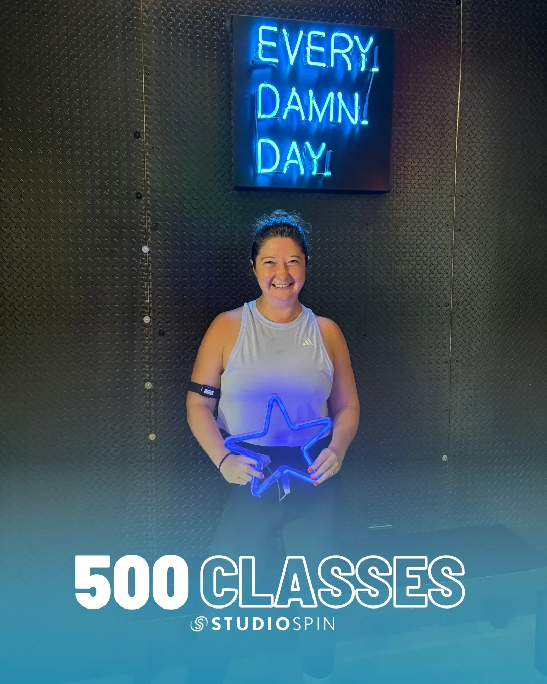 A Studio Spin member celebrating 500 classes under the Every Damn Day neon sign.