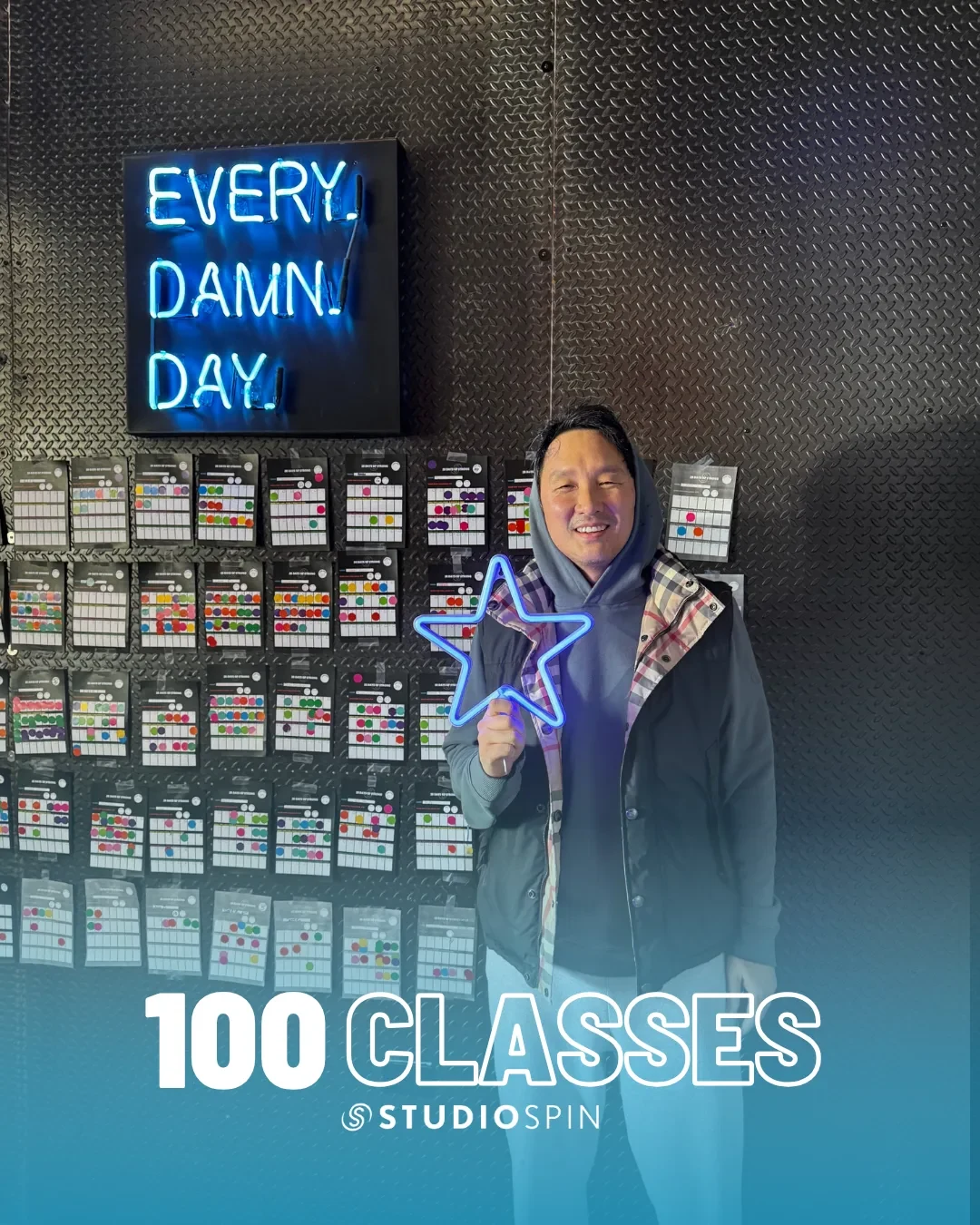 A Studio Spin member celebrating 100 classes under the Every Damn Day neon sign.