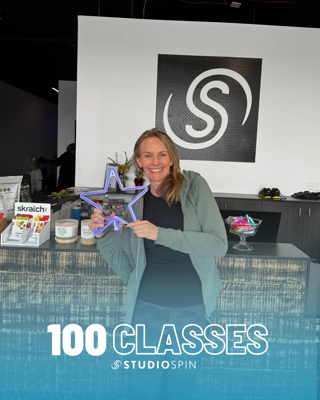 A Studio Spin member celebrating 100 classes under the Every Damn Day neon sign.