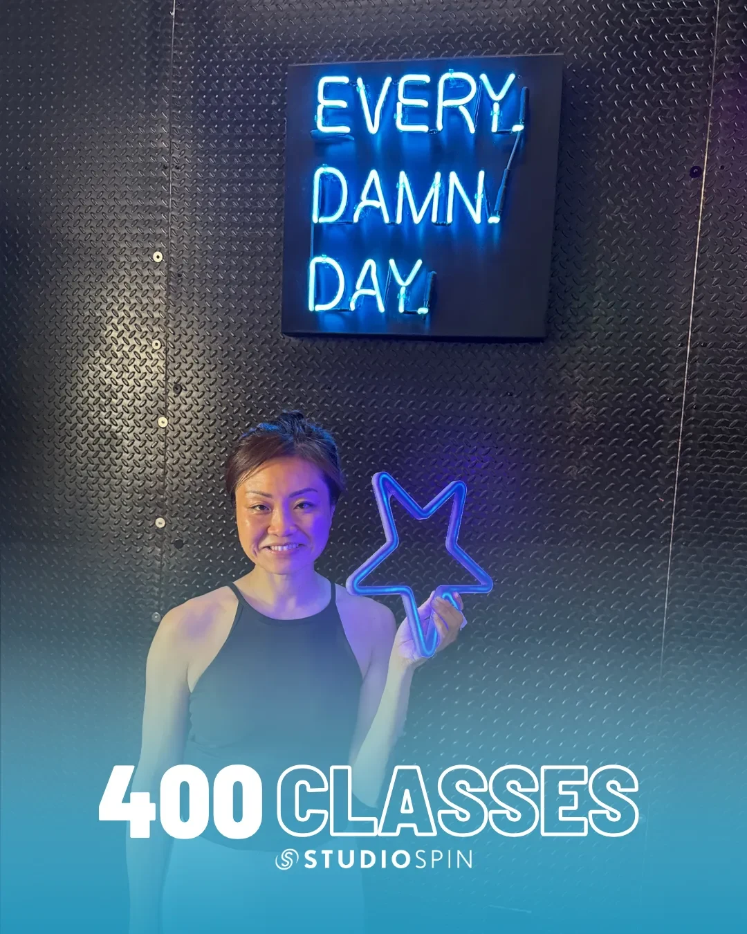 A Studio Spin member celebrating 400 classes under the Every Damn Day neon sign.